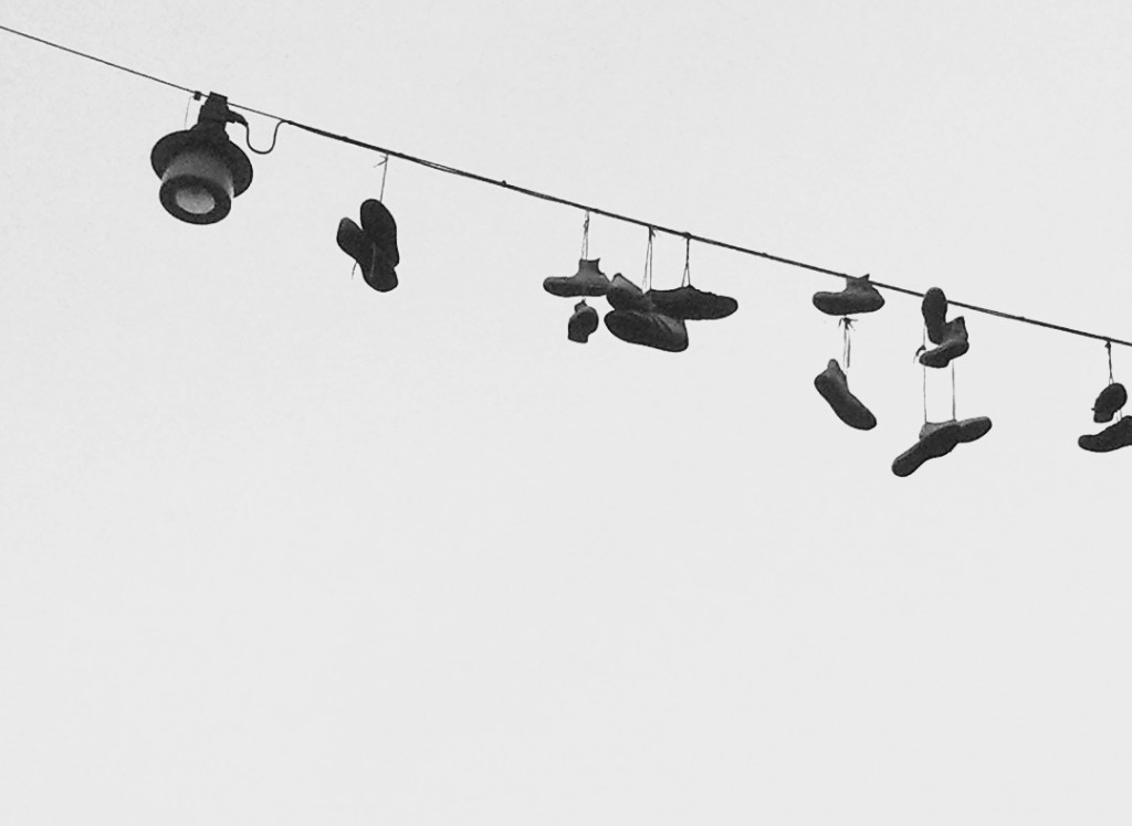 Mehrere Paar Schuhe hängen an einer Stromleitung, links ist eine Straßenlaterne zu sehen.